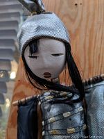 Close-up of the mermaid's face showing painted simple features, red lips, black hair, and a metallic silver fabric hat.