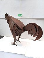 Side angle view showing detailed wing, tail feathers, and body shape of rusted metal rooster sculpture.