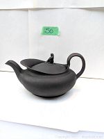 Side view of oval black teapot with woman figure on lid and curved handle