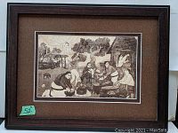 Framed limited edition print titled La Comide depicting traditional Mexican village scene with women preparing food outdoors, dark wood frame with textured brown mat.