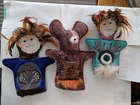 Photo showing three handmade puppets laid out on white cloth with visible feather decorations and detailed fabric appliqué.