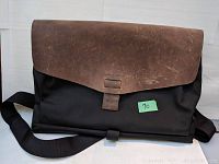 Front angled view of the black nylon computer satchel with brown leather front flap and adjustable shoulder strap.