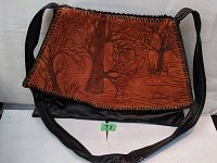 Full front view of brown leather purse featuring embossed Trees of Life design and wooden whipstitch edge, with long black leather strap attached.