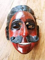 Close-up photo of the early 20th century ceremonial dance mask from Michoacan, Mexico, showing hand carving, painted features, and detailed mustache and hair.