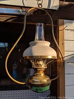 Side view of antique hanging oil lamp showing ceramic shade, glass chimney, and brass frame hanging from chain