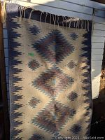 Entire rug hung vertically on slatwall, showing full geometric diamond design and fringe.