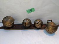 Four antique horse sleigh bells of varying sizes attached to a worn leather strap, displayed against a white background with a green lot tag '99'.