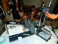 Wide view of Yardworks electric chainsaw, microwave flower press kit with instructions, and metal drill press frame on table.