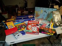 Photo showing multiple boxed board and card games including Parcheesi, Yahtzee, Mastermind, Flits, Memory, Magnetic Chess, and Mixed Up on a white table.