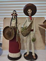 Front view of male and female Day of the Dead skeleton figures, showing detailed clothing and accessories.