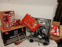 Full view of tools including Workmate bench and toolbox, stud driver with metal case, boxes of studs and cartridges, rivet tool, and corded drill.
