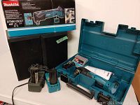 Makita cordless multi tool with its carrying case, instruction manual and accessory package, two Makita batteries and chargers shown next to the case