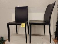Front view of two black leatherette dining chairs, showing clean design and upholstery condition.