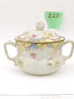 Front view of bone china lidded teacup showing two handles, floral hand-painting, and gold detailing