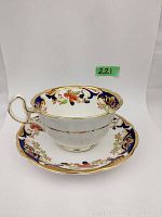 Side view of teacup on saucer showing detailed floral hand painting, cobalt blue and gold trim