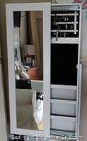 Full view of closed jewelry cabinet with mirrored front reflecting surrounding room.