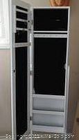 View showing full height white jewellery cabinet door fully open revealing black velvet interior with various compartments for rings, earrings, necklaces, shelves, and tilt mirror on inner door.