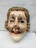 Front view of the hand-carved wooden Pastorela dance mask showing mustache, curled hair, painted facial details.
