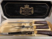 Open box with carving knife, fork, and sharpening steel inside showing handles and blade markings.