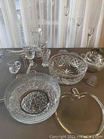 Overview of various crystal bowls, glass vases, and decorative glass pieces on a dark surface against a sheer curtain background.