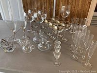 Wide shot of entire collection showing variety of glassware and stemware on a table with wood-paneled background.