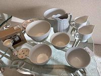 Photo of white ceramic bowls and pitchers on a glass top table, showing size variation and shapes.