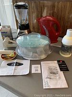 Full view of the kitchen small appliances including blender, red kettle, food steamer with trays and lid, and food chopper with accessories on table.