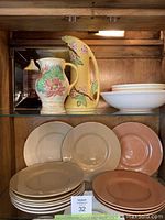 Shelf with two vintage ceramic jugs with floral designs and stacks of Retroneu Everyday stoneware plates in beige and pink.