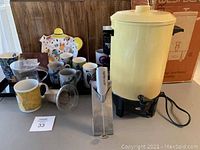 Westbend coffee maker with original box, Aero latte frother, and various coffee and tea cups on a table.
