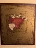 Framed wall art piece showing red bowl with white cup and white blossoms on olive green background, wood frame, some surface damage visible