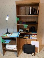 Full view of oak bookshelf with shelves and cabinet next to wooden rolling table with office items on top and lamp attached