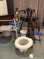 Photo showing walkers, canes, raised toilet seat, commode chair, bucket, and sock aid device grouped together.