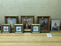 Seven framed art pieces on a shelf, varying sizes and wood-tone frames.