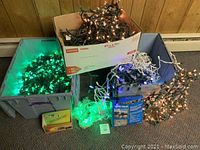 Boxes and bins filled with tangled green, blue, and multi-colored Christmas lights placed on the floor against a wood-paneled wall