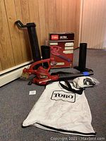 Full lot of Toro Ultra electric blower vac parts including tubes, bag, box, and control tag in a room with wood panel walls.