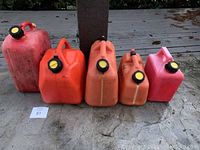 Photo of five plastic gas cans ranging from very small to large, all orange-red color with black and yellow caps, placed on outdoor concrete surface.