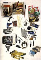 Overview photo showing paint brushes, scrapers, glue gun, paint rollers, scrapers, wire brush, zip ties, and other small hand tools arranged on a white surface.