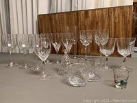 Full view of all items including six stemmed wine glasses, two water goblets, cream and sugar set, crystal bell and small shot glass arranged on a surface