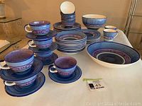 Full lot view showing dinnerware set including plates, bowls, cups, and saucers in blue and purple colors.
