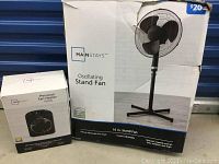Two boxed Mainstays products: a large box containing the 16-inch oscillating stand fan and a smaller box containing the personal fan heater.