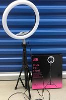 Photo of one LED ring light mounted on adjustable tripod in front of blue backdrop next to the product box showing packaging design.