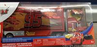 Front view of boxed red metal transport truck toy featuring Lightning McQueen artwork and number 95, showing toy inside packaging.