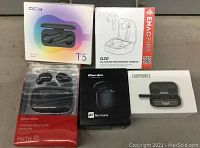Lot of 5 different wireless earbud boxes and packages, showing brands QCY, ENACFIRE, Bluedio, and generic wireless earphones.