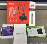 Full lot displayed showing MPOW TH1 Bluetooth headset box, selfie stick tripod box, two wireless earbuds box, white wireless headset box, and EBL USB charger box.