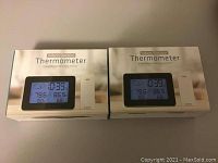 Two boxed indoor outdoor thermometers shown in their retail packaging with digital display visible.