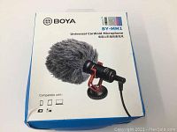Box featuring BOYA BY-MM1 Universal Cardioid Microphone branding and compatibility icons for smartphone, camera, and laptop.