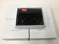 Five boxed Linpa World wireless earpieces shown stacked with one charging case visible open showing the earpieces inside.