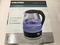 Photo of Kalorik cordless glass kettle in original retail box highlighting product features such as 1.7L capacity, blue LED illumination, and cordless 360-degree base.