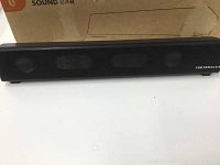 Front view of the black Taotronics soundbar with metal grille and brand logo visible. Box in background.