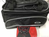 Black multi-storage zipper bag with shoulder strap and front zip compartment labeled Lixada, shown with a red and black radio.